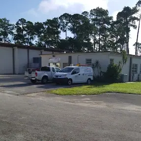 A side view of a brick building. A pickup truck and a delivery vehicle are parked in front of the building.