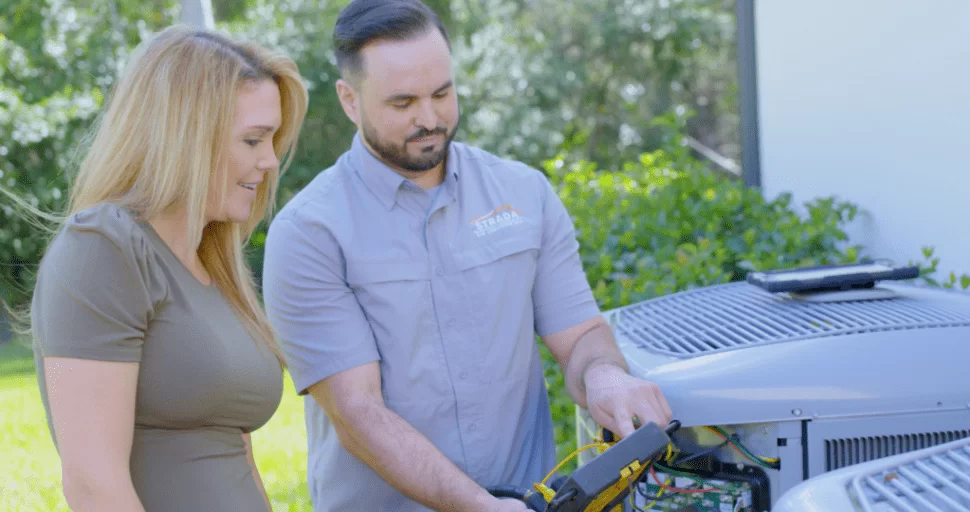 Strada Services technician working on HVAC system outside and talking with homeowner