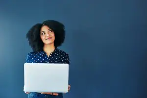 Woman holding laptop looking up thinking on blue background
