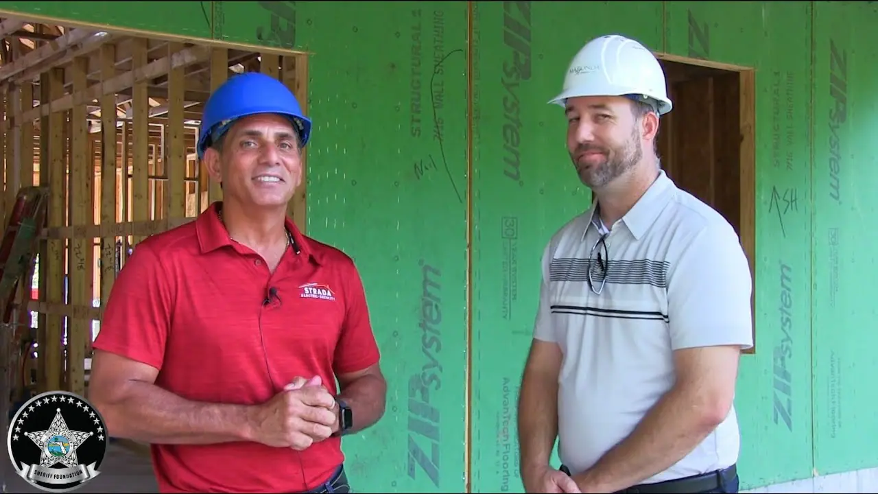 Two men are smiling and wearing hardhats in a construction zone. There's a silver star logo for the Sheriff Foundation.